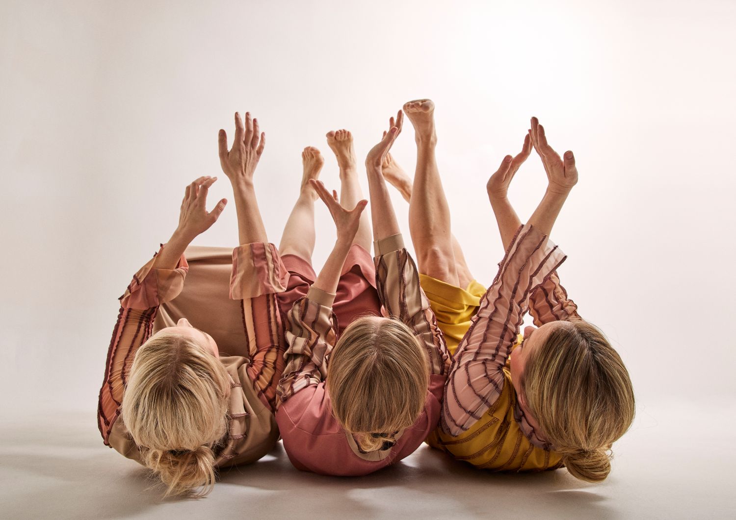Tre dansare ligger på golvet och sträcker sina händer mot taket.