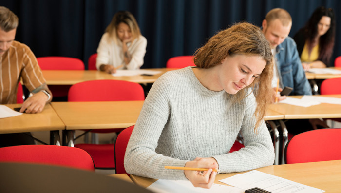 Student som sitter i ett klassrum tillsammans med andra studenter och antecknar