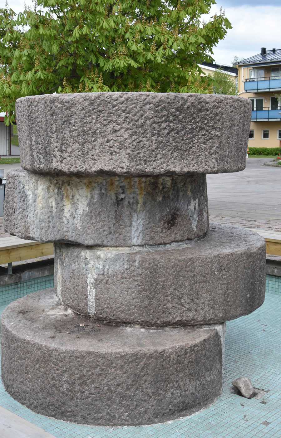 Fyra kvarnstenar ojämnt staplade på varandra i en bassäng. 