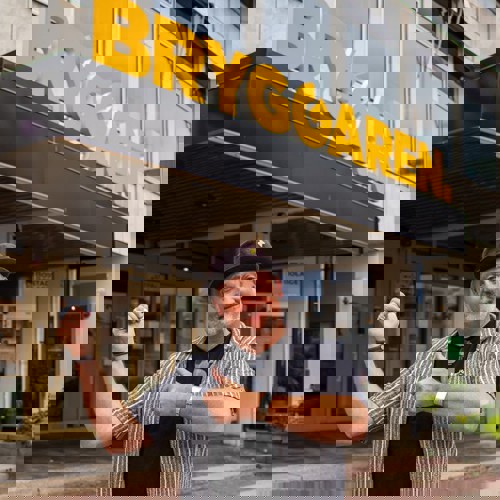 Tobias utanför Bryggaren som pekar på Bryggarens gula skylt.