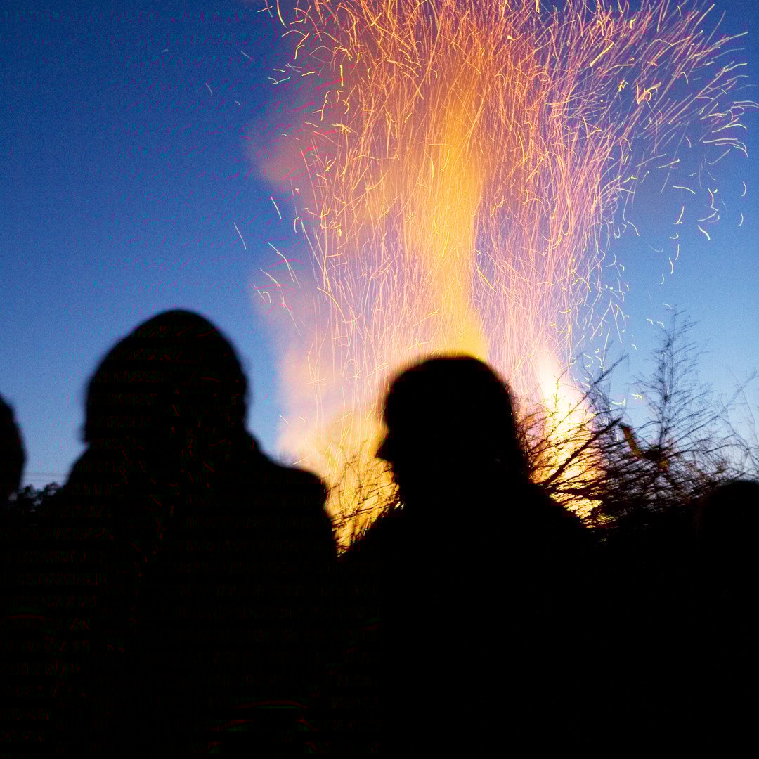 Människor som står framför brinnande valborgsmässoeld. 