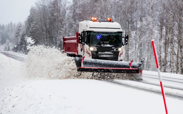 Plogbil som kör på en igensnöad väg. 
