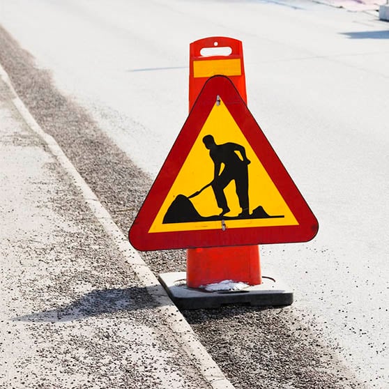 Vägskylt för vägarbete. En gul triangel med röd ram i och en person som står och gräver. 